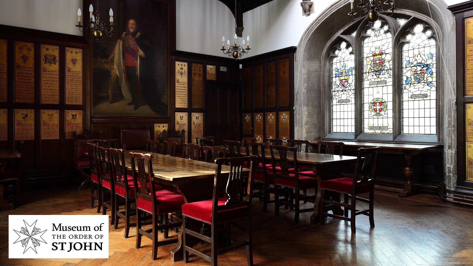 Photograph of a panelled room with a portrait oil painting on one wall and stained glass windows in another.
