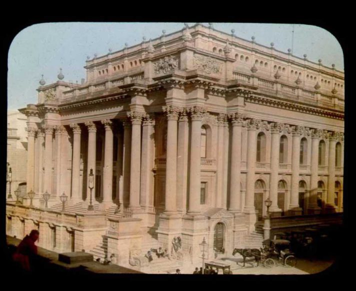 exterior of Royal Opera House in Malta with people sitting on steps and numerous horse-drawn carriages"