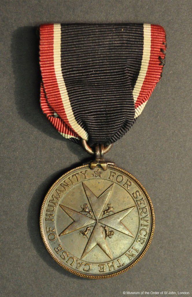 A round bronze medal with a central eight-pointed cross with unicorn and lion supporters with writing in a border, suspended from a black, red and white ribbon.