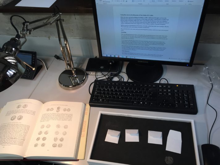 A desk with computer and open book, and four coins in a tray