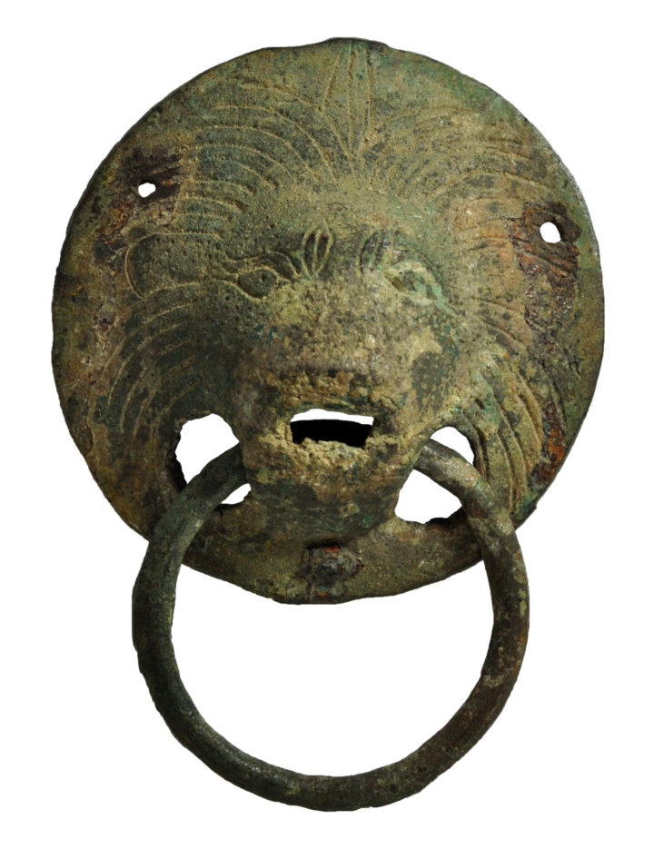 A metal ring hanging from a piece of metal with the face of a lion engraved in it.