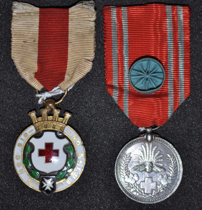 Left hand medal round with white rim bearing an inscription. Crown on top and shield in middle. On a white and red ribbon. Right hand medal a round silve coloured medal with a cross and flora on it. Red and white ribbon with blue button in middle.