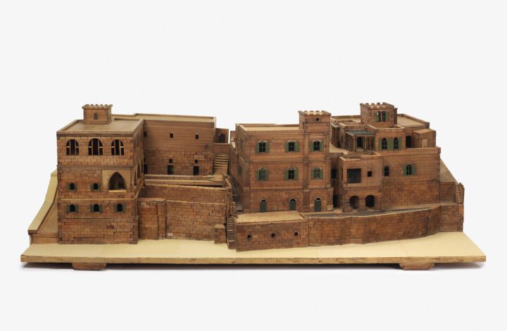An overall front view of a wooden model of a hospital building with brick detail, windows, walkways and staircases.