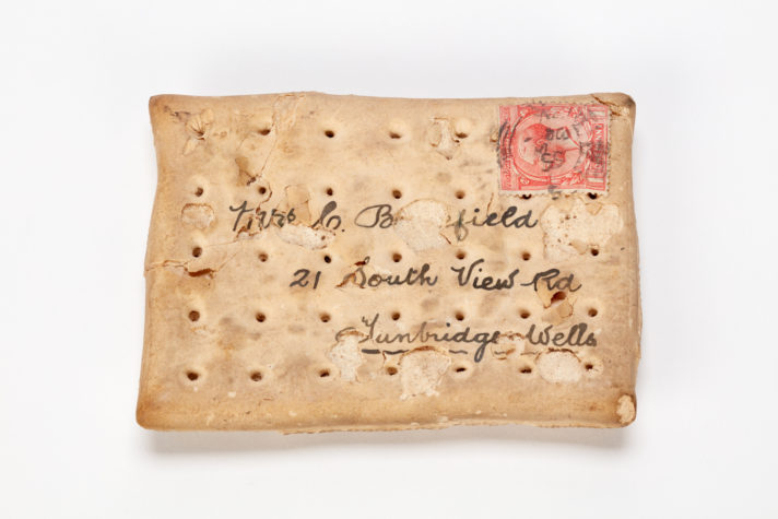 Photograph of a rectangular cracker-type biscuit with an address written on it in ink and a stamp in the top righthand corner.
