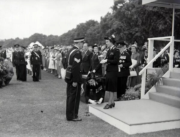 A black and white photograph with John Price in his Cadet Corporal Uniform recieving the American Cup for Gallantry from HRH Princess Margaret who is stood on a white plinth at the bottom of some steps wearing her ceremonial St John Ambulance Uniform holding the cup in white, gloved hands.