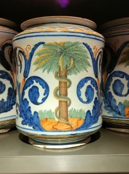 ALT="a glazed ceramic pharmacy jar with a design of a serpent around a tree with blue feathers on either side"