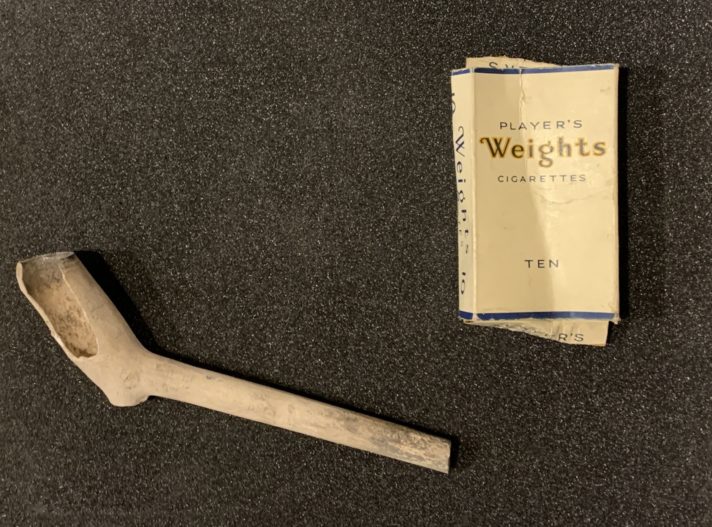 ALT="Cream coloured clay smoking pipe with piece missing from bowl on right, cream card box with text reading 'Players' Weights Cigarettes' '10'"