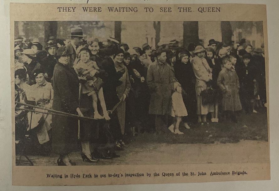 A close-up photograph of one of the newspaper cuttings in the scrapbook, showing civilians waiting to see the Queen.