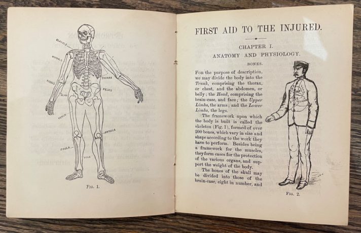 This image is of a double-page spread from the publication. The left-hand page shows an illustration of a skeleton, with some of the key bones identified with their scientific term. The right-hand page is titled ‘First aid to the injured’ and ‘Chapter 1 Anatomy and Physiology’, and begins to explain the framework of the body. It is accompanied by a full-length illustration of a clothed man, facing left.