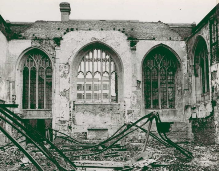 Black and white image of the Priory Church after bombing with walls and windows intact, but rubble in interior and no remaining roof.