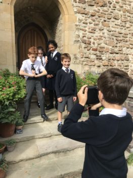 Four children pose on some stone steps in front of the Church wall while a fifth child takes a photograph.