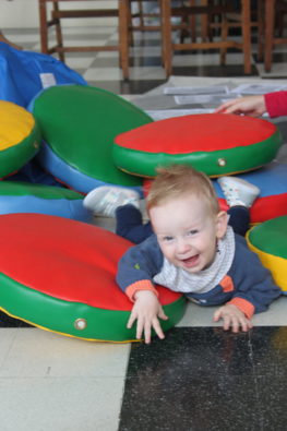 A happy toddler lays on a pile of colour cushions.