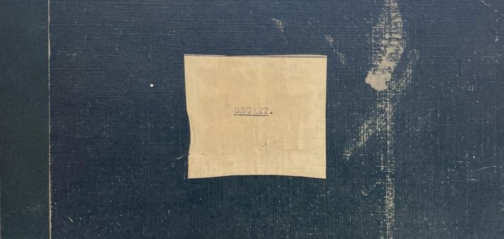 Cropped image of a navy ring binder with a note on the cover stating the contents are 'secret'