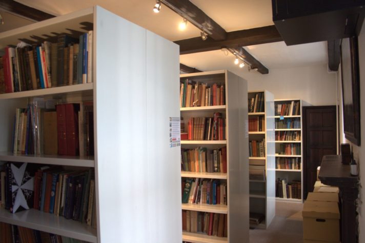 A historic room is filled with metal shelves, upon which modern books are neatly arranged.