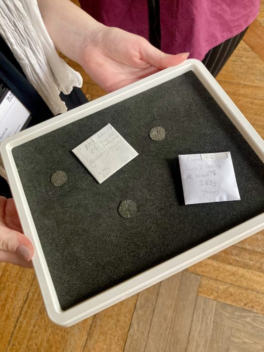 A black tray held out by Ilenia, containing three coins and two white square coin envelopes. 