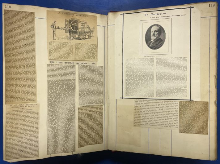 A large scrapbook lies open on a blue table. The pages contain cuttings of textual articles with some accompanying black and white photographs from old newspapers.