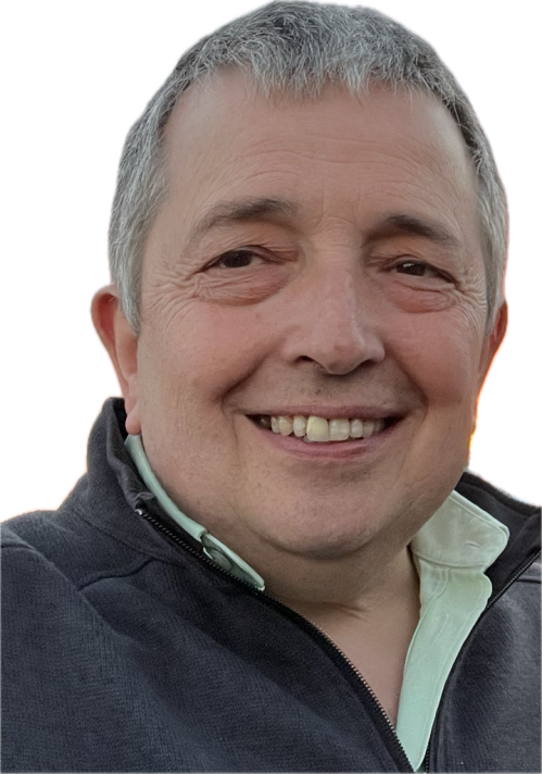 A colour head and shoulders colour photograph of a white man with short grey hair. He is wearing a dark coloured fleece, and visible under it, a white shirt. He is looking towards the photographer and smiling.