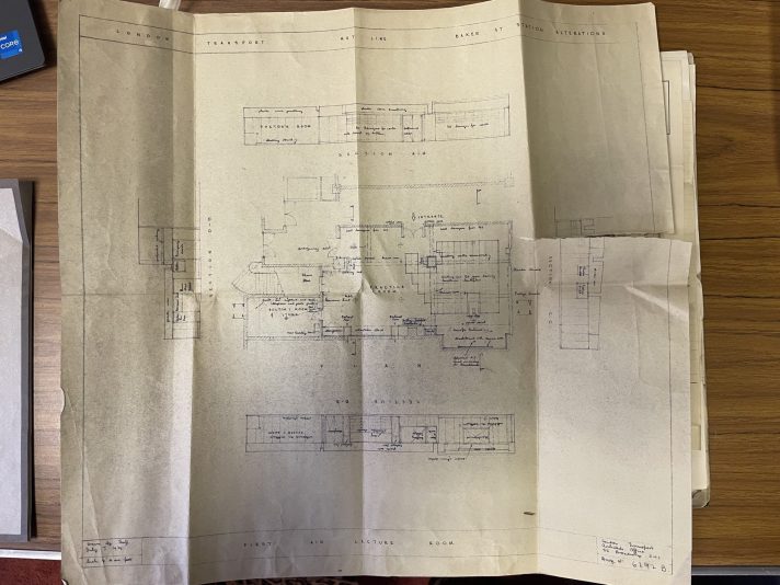 A large, square document is open no a table. The document is an architectural plan of a building, and features a detailed line drawing of the building. 